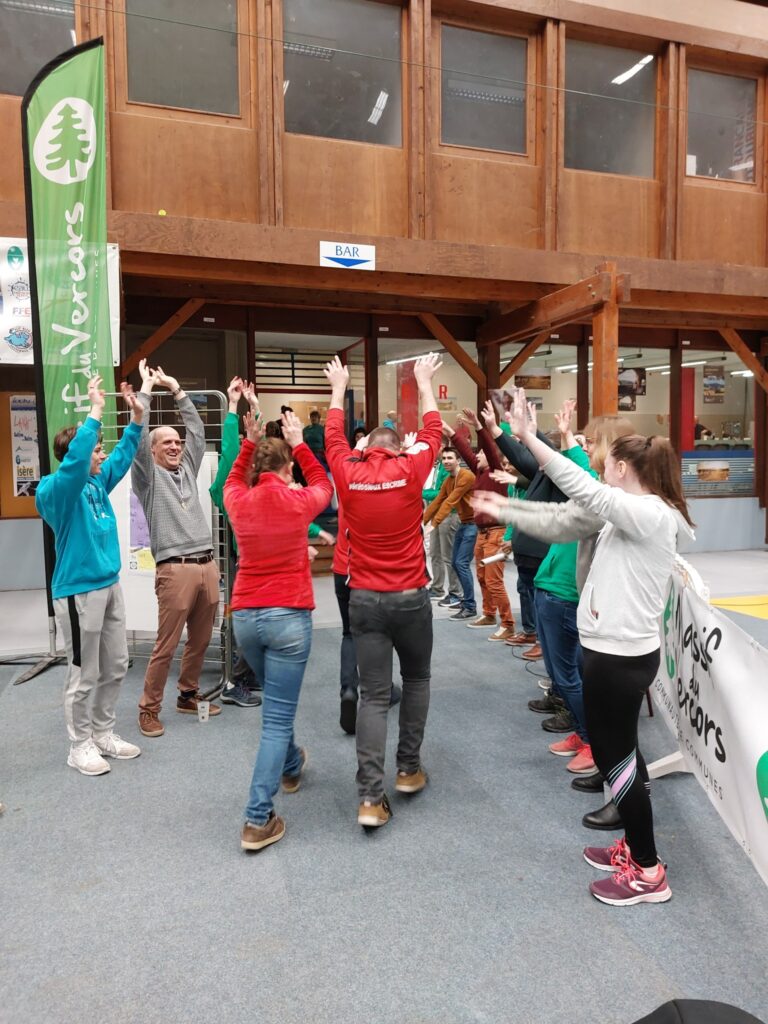 Un groupe d’adultes et d’adolescents en deux rangées face à face, bras levés, sous les banderoles du Vercors.