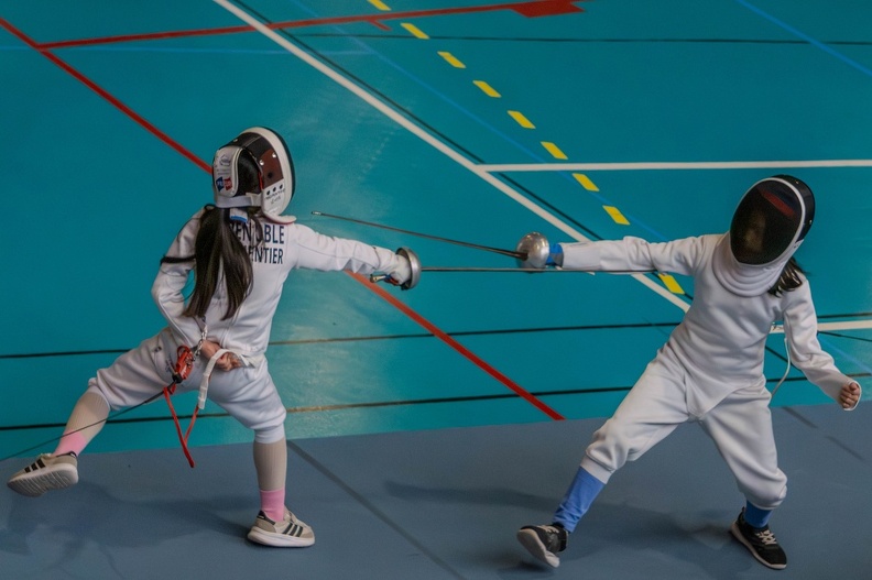 Deux jeunes tireuses en fente, fleuret en main, sur la piste du gymnase