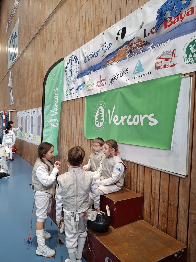 De jeunes fleurettistes assis sous la bannière de la Vercors Cup et du tournoi Bayard, entourée des logos des partenaires du massif.