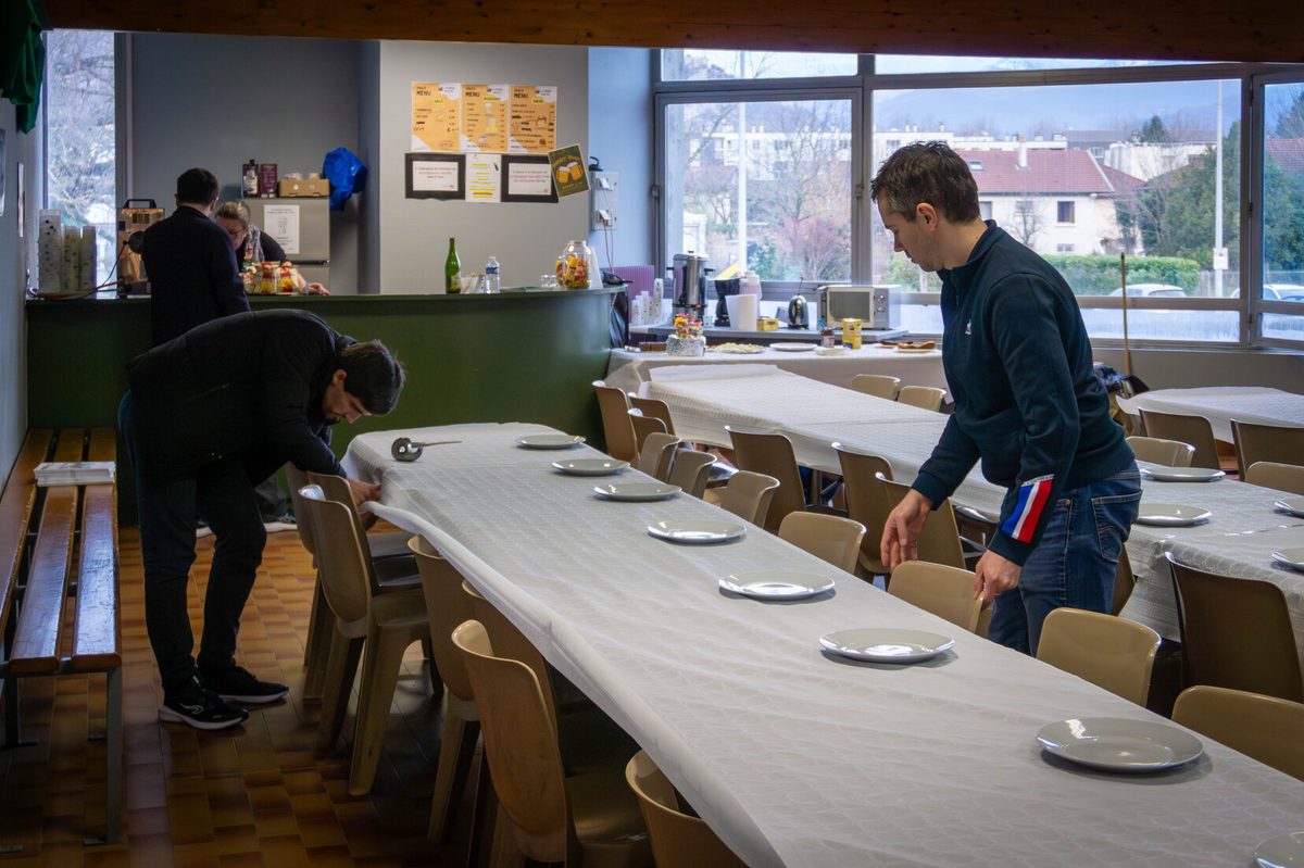 Deux bénévoles nappent les longues tables et disposent les assiettes avant le repas du soir