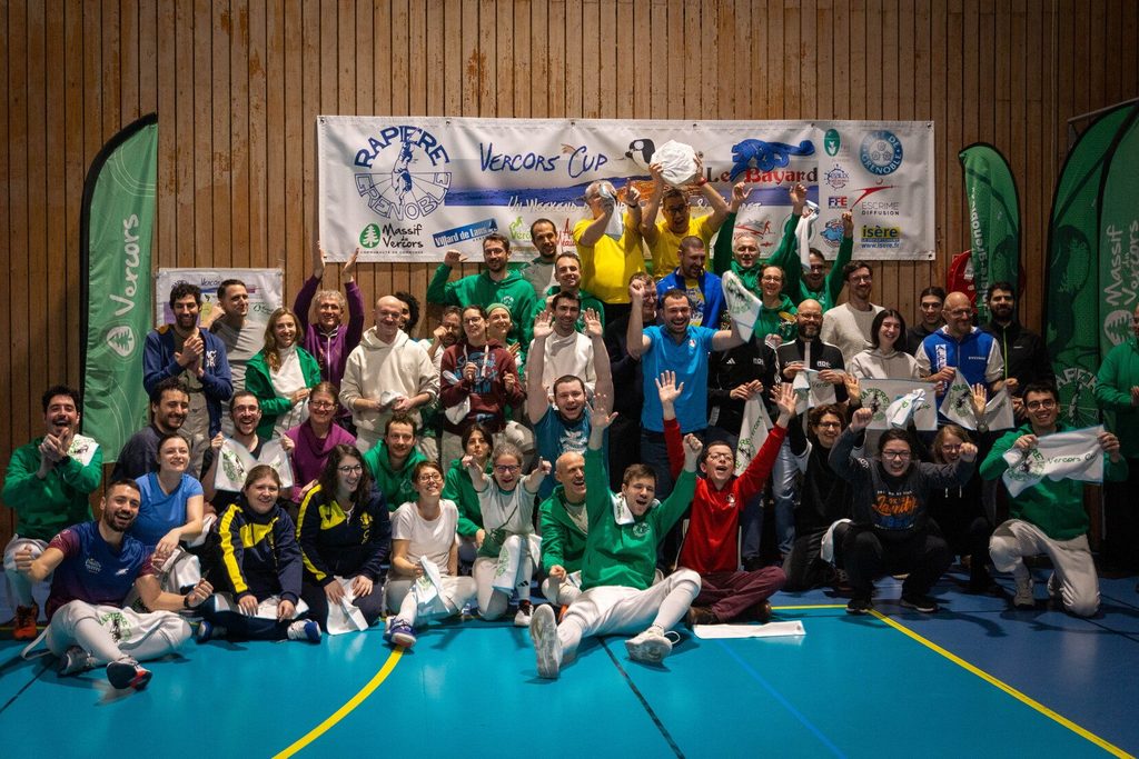 Photo de groupe à la fin de la Vercors Cup 2026 : tous les tireurs réunis sous la bannière, la meule de bleu brandie au-dessus des têtes.
